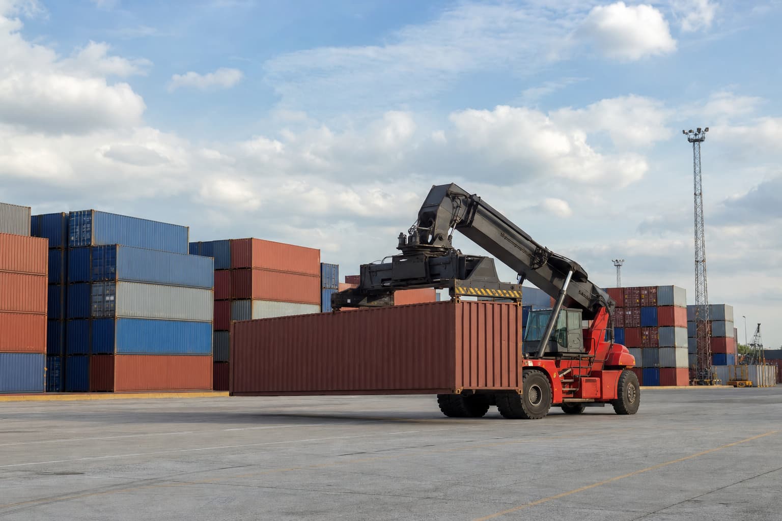 A reach stacker lifting a plain freight container in a working yard